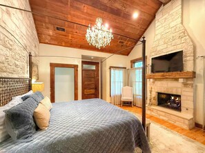 Un dormitorio con cama, candelabro, chimenea y televisor.
