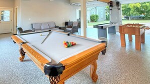 A pool table with a foosball table and seating area in a spacious room with a view of the outdoors. - Herber Haus, Historic Luxury • Walk to Main • Game Room (Fredericksburg)