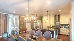 A spacious dining area with a wooden table and chairs, a kitchen with white cabinets, and a hanging light fixture. - Herber Haus, Historic Luxury • Walk to Main • Game Room (Fredericksburg)