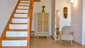 Un escalier en bois mène à une pièce où se trouvent un meuble en rotin, une chaise et un luminaire fixé au mur.