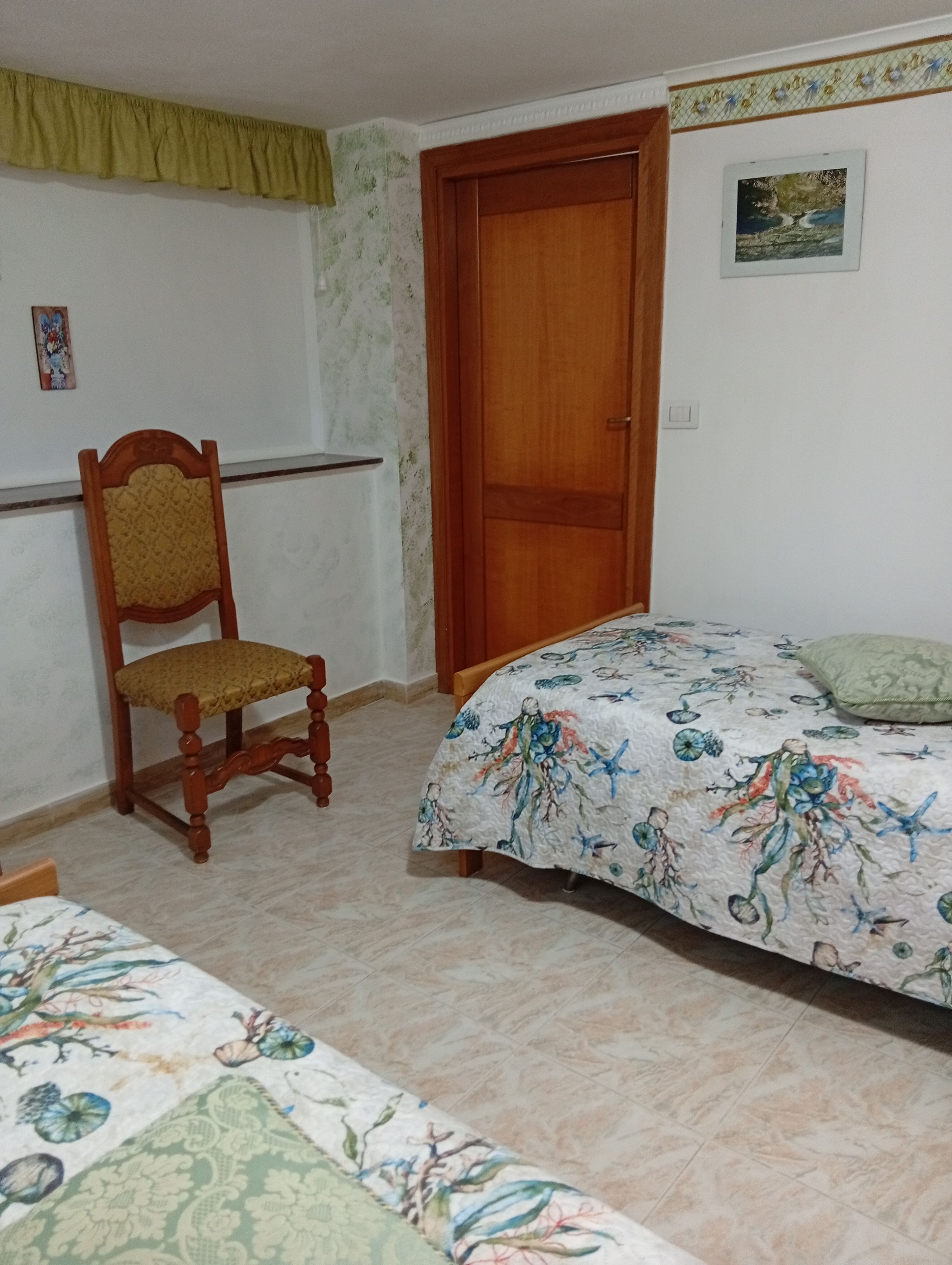 A bedroom with a bed, a wooden chair, a door, and a small painting on the wall.