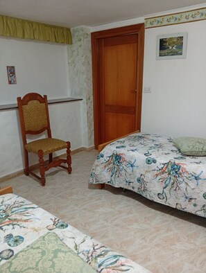A bedroom with a bed, a wooden chair, a door, and a small painting on the wall. - LA CORTE CASA VACANZE - NEAR ALGHERO-STINTINO (Località La Corte)