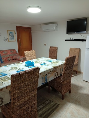 Un área de comedor con una mesa, sillas, un sofá, un televisor y un equipo de aire acondicionado.