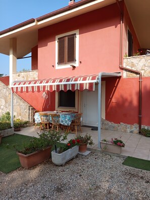 Un bâtiment rouge avec un patio couvert, une table entourée de chaises et des plantes en pot.