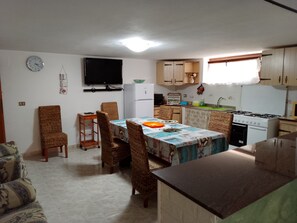 A compact kitchen with a dining area, a flat-screen TV, and a clock on the wall. - LA CORTE CASA VACANZE - NEAR ALGHERO-STINTINO (Località La Corte)