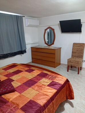 Une chambre à coucher comprenant un lit, une commode, une chaise, un miroir et un téléviseur à écran plat fixé au mur.