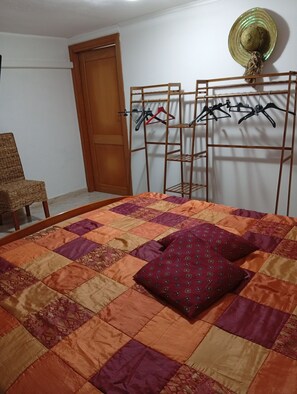 Un dormitorio con cama, una silla de madera, un armario y un tendedero.