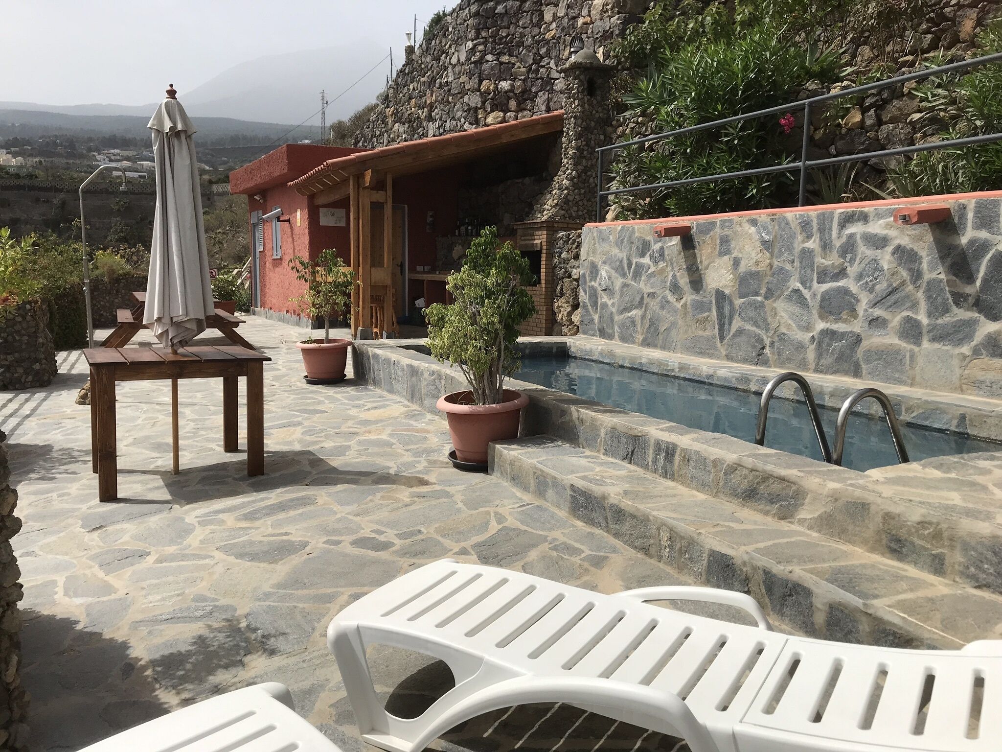 A stone patio with a pool, outdoor seating, and potted plants.