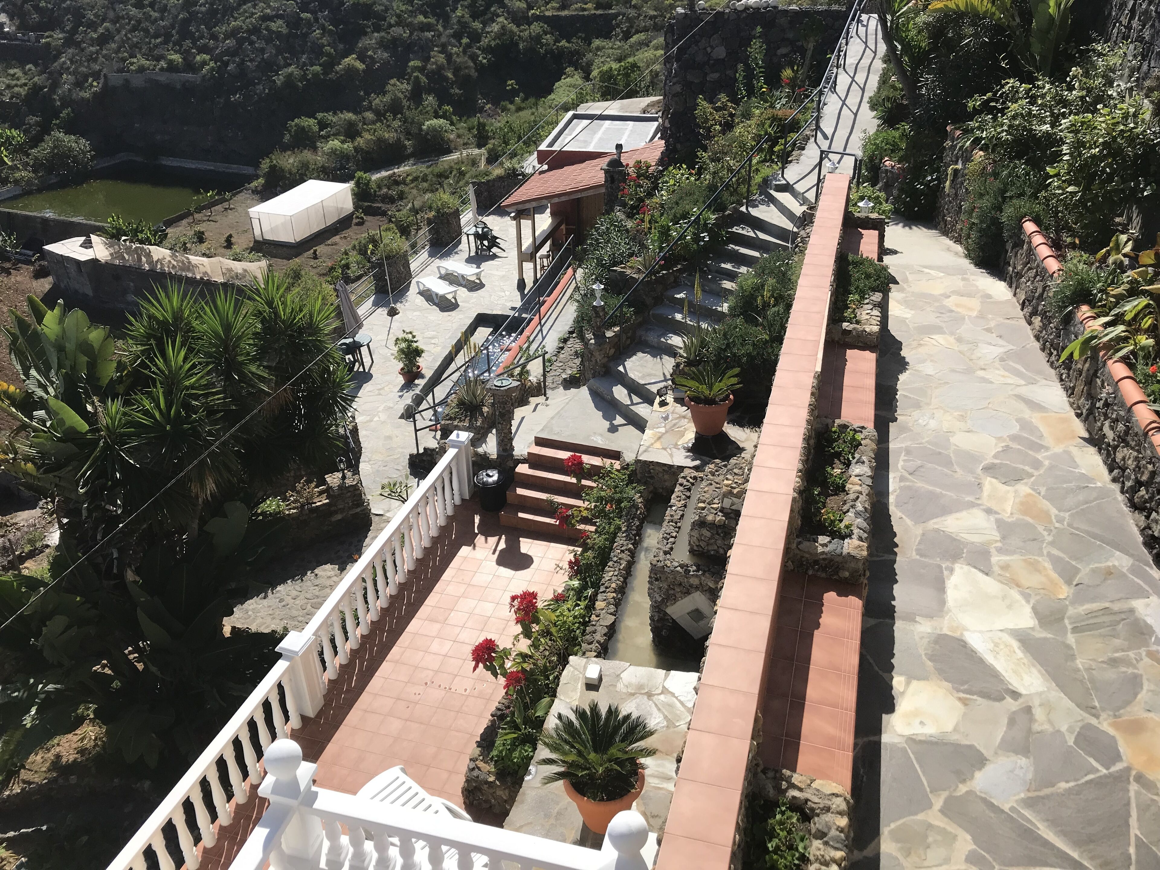 A multi-level outdoor terrace with stone flooring, potted plants, and a water feature.