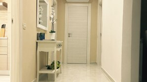 A hallway with a white door at the end, a small shelf with a plant, and a mirror above the shelf.