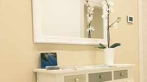 A white console table with a mirror above it, a small potted plant, and a framed picture on the table.