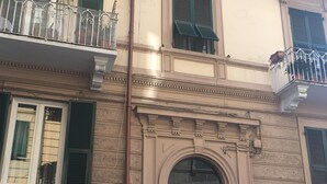A building with a classic architectural style, featuring a central entrance with an arched doorway, green shutters on the windows, and balconies with metal railings.