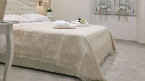 A bedroom with a bed, a bedside table with a lamp, a window with curtains, and a small potted plant.