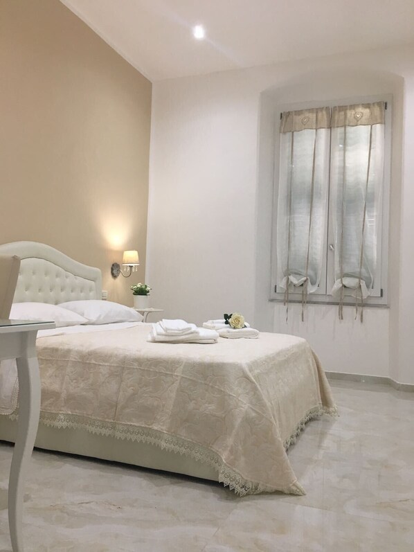 Una camera da letto con un letto, un comodino con una lampada, una finestra con tende e una piccola pianta in vaso.