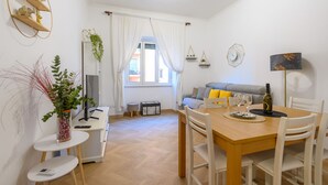 A modern living room with a sofa, a dining table with chairs, a TV, and a window with curtains. - Barsanti Apartment (Roma)