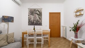 A dining area with a wooden table and white chairs, a wall-mounted air conditioner, a door, and a radiator. - Barsanti Apartment (Roma)