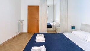 A hotel room with a bed, a wooden door, a mirror, a nightstand, and a lamp. - Barsanti Apartment (Roma)