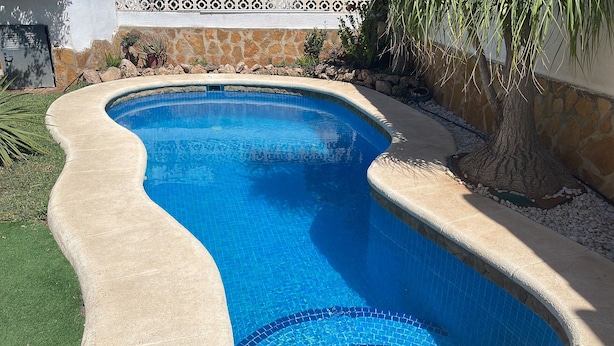 Ein bogenförmiger Swimmingpool mit einer Steinmauer und einem Zierzaun.