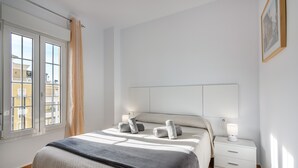 Een slaapkamer met een bed, twee nachtkastjes, een raam met gordijnen en een aan de muur hangend schilderij.
