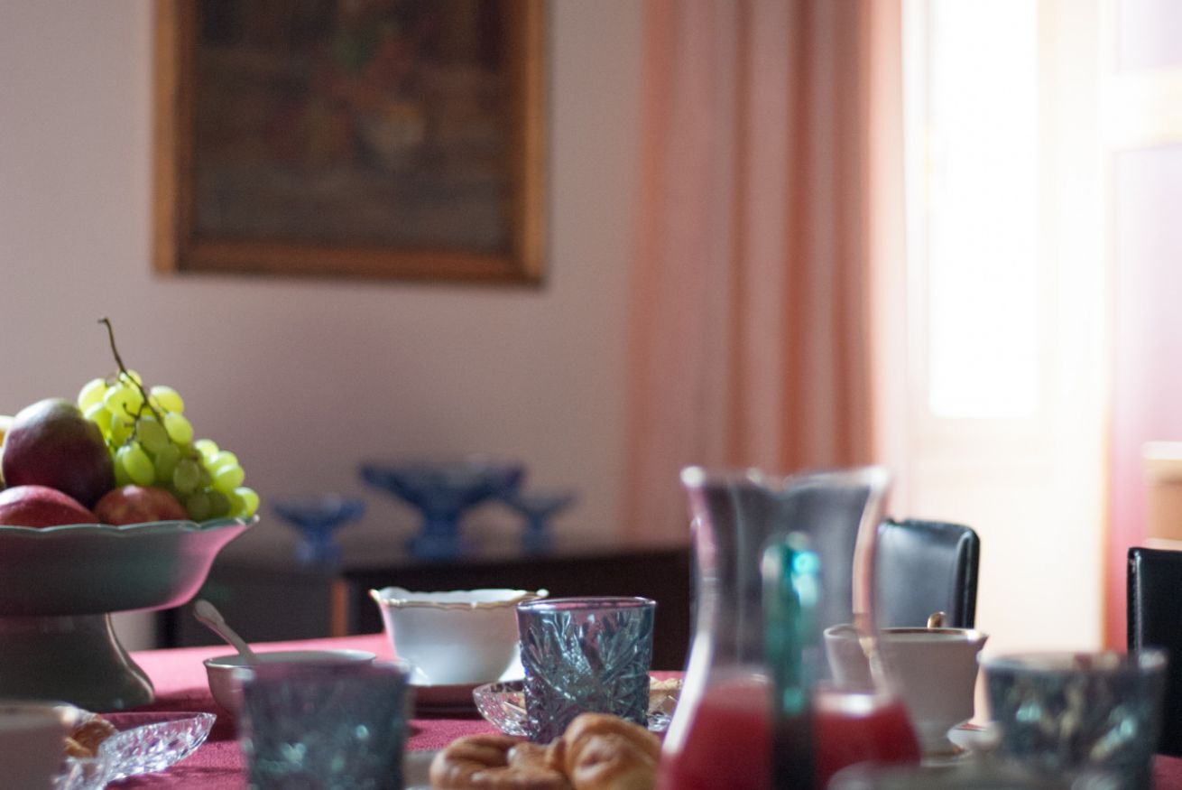 A dining table with a bowl of fruit, a pitcher, and various glassware.