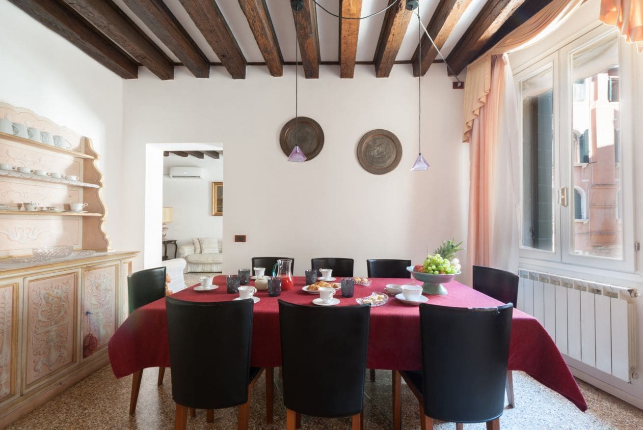 A dining area with a red tablecloth, black chairs, and a wooden ceiling.