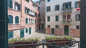 A narrow street with buildings on either side, featuring balconies with plants and a central open space.