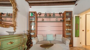 A room with a green dresser, a white table, a striped sofa, and a bookshelf with decorative items.