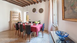 A dining area with a red tablecloth, wooden chairs, a fruit bowl, and a vintage cabinet.
