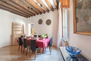 A dining area with a red tablecloth, wooden chairs, a fruit bowl, and a vintage cabinet.