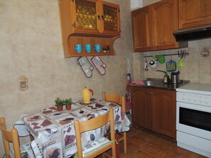 Une cuisine avec des meubles de rangement en bois, une cuisinière et une table recouverte d’une nappe à motifs de café.