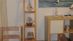 Ein Essbereich mit einem Holztisch, Stühlen, einer Kerze und einem Bücherregal mit maritimer Dekoration.