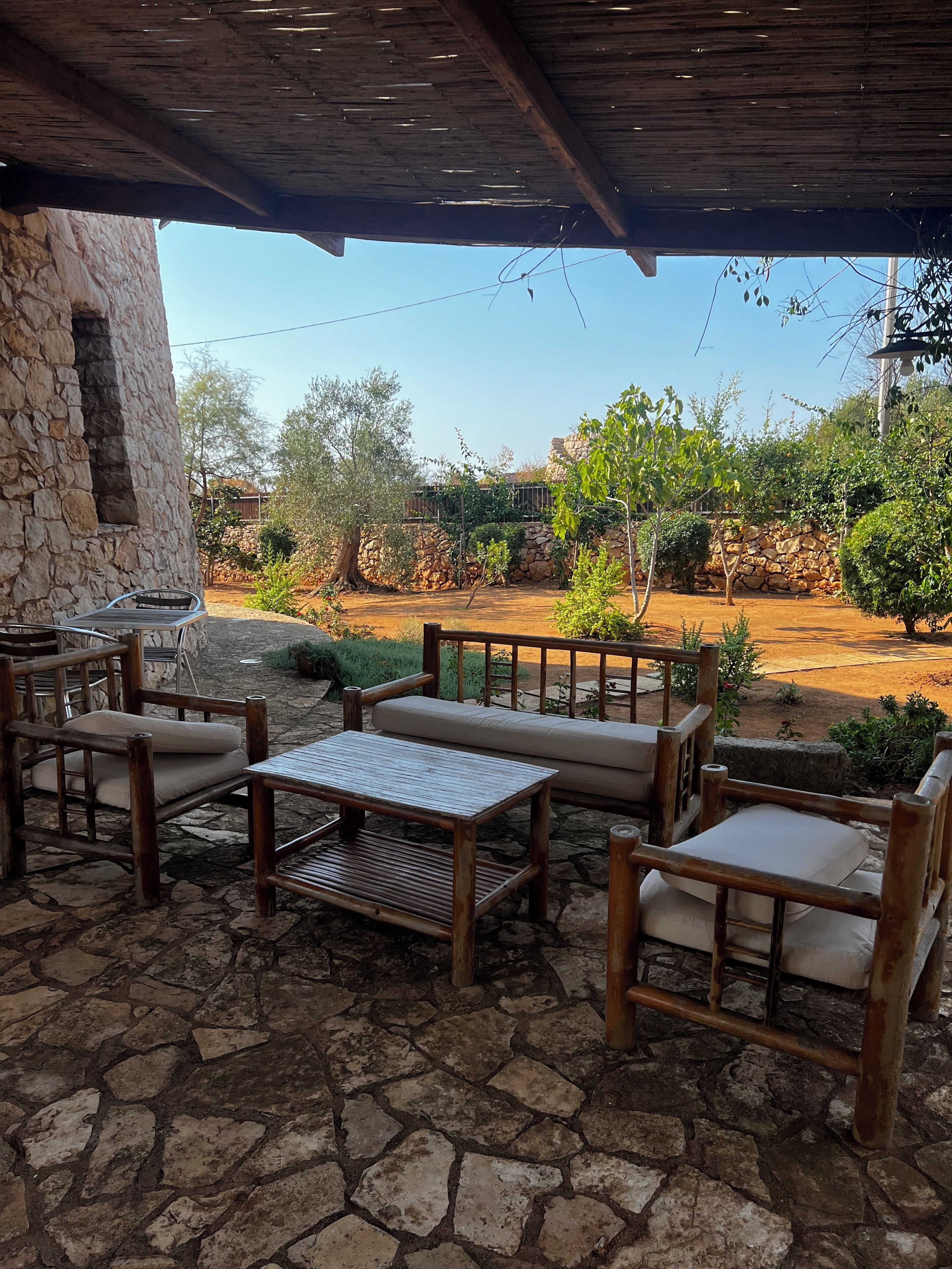 An outdoor patio with stone flooring, wooden furniture, and a stone wall.