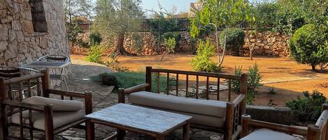 An outdoor patio with stone flooring, wooden furniture, and a stone wall.