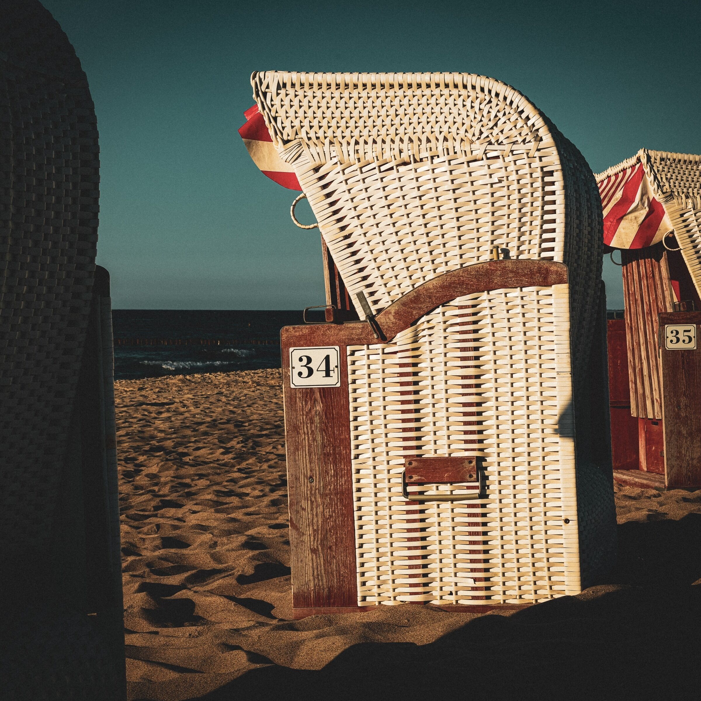 Deux chaises de plage, numérotées 34 et 35, un poteau en bois et une plage de sable avec l’océan en arrière-plan.