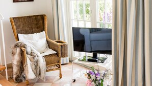 A cozy living room with a wicker chair, a sofa, a coffee table with a book and flowers, and a TV. - Small coach house: 10 min. to the beach, in the middle of nature, sauna & whirlpool (Klein Bollhagen)