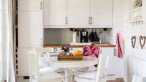 A kitchen with white cabinets, a dining table with chairs, and a fruit basket. - Small coach house: 10 min. to the beach, in the middle of nature, sauna & whirlpool (Klein Bollhagen)