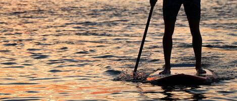 A person paddleboarding at sunset with the sun setting on the horizon.