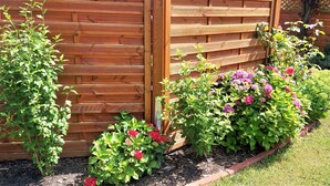 Een tuin met een houten omheining, diverse bloeiende planten en een verzorgd gazon.