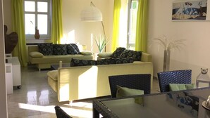 A living room with a sofa set, a dining table with chairs, and a large window with curtains. - Holiday house in the nature reserve Schwalmtal  (Schwalmtal)