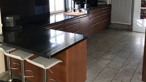 A modern kitchen with a black countertop, wooden cabinets, and a central island with bar stools. - Holiday house in the nature reserve Schwalmtal  (Schwalmtal)