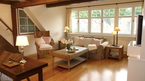 Ein gemütliches Wohnzimmer mit einer Holztreppe, Korbmöbeln und einem großen Fenster mit Jalousien.