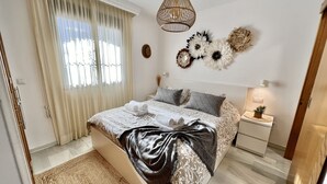 Une chambre à coucher bien aménagée, avec un lit, des tables de chevet, un luminaire suspendu et des œuvres d’art décoratives au mur.