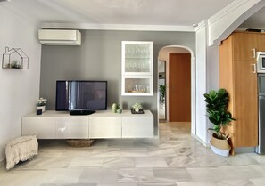 A modern living room with a flat-screen TV on a white console, a glass display cabinet with decorative items, and a potted plant. - 43 - Apartment with large terrace in El Faro, Mijas (Mijas Costa)