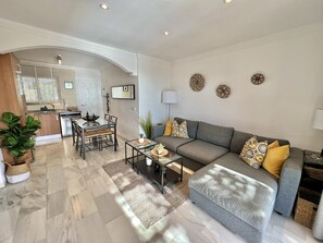 A modern living room with a grey sofa, a coffee table, and a dining area with a glass table and chairs.