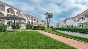 A courtyard with a pathway, white buildings with arched balconies, and a palm tree.