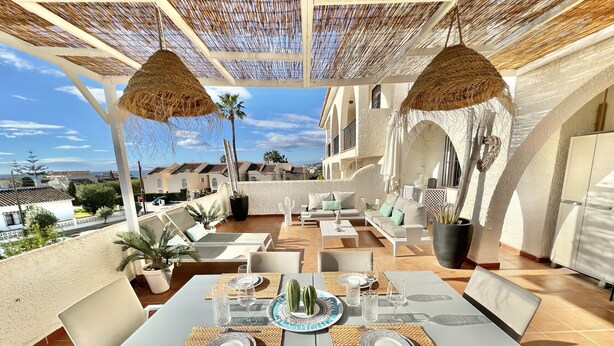 Une terrasse extérieure avec des meubles blancs, une table dressée pour le repas et une vue sur le paysage urbain.