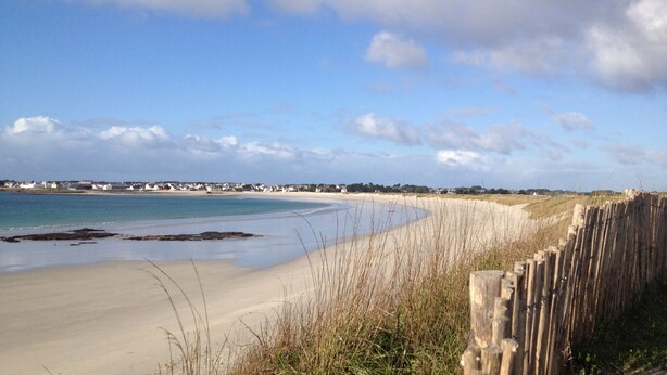 A beach with a wooden fence, sandy shore, and houses in the distance. - Asian pavilion one minute from the beach (Loctudy)