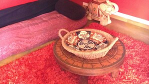 A room with a red cushioned bench, a small table with a decorative tray, and a vintage-style lamp. - Asian pavilion one minute from the beach (Loctudy)