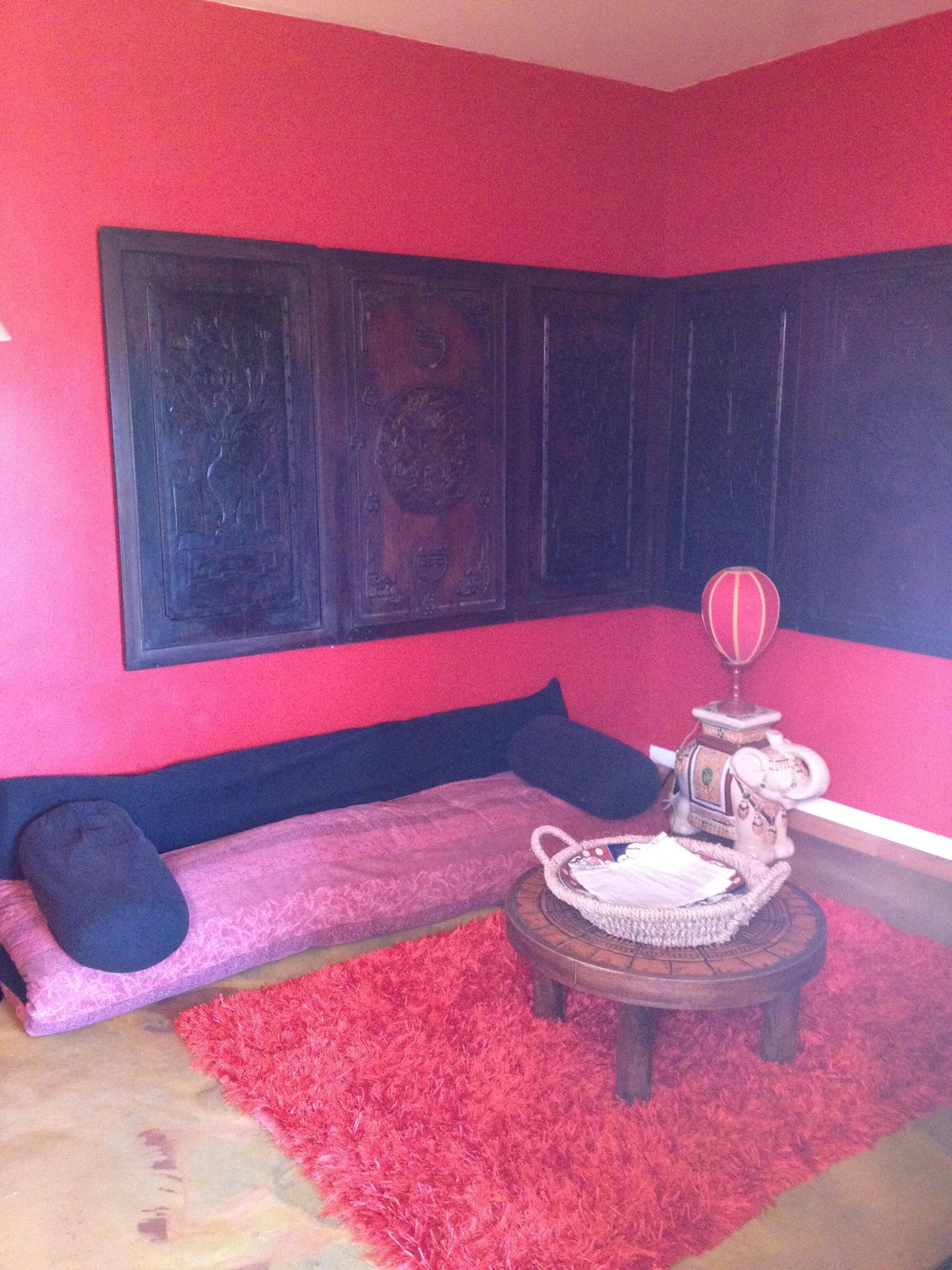 Une pièce avec une moquette rouge, un canapé avec des coussins foncés, une petite table ronde agrémentée d’un objet décoratif et une grande œuvre d’art encadrée accrochée au mur.