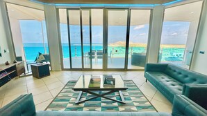 A spacious living room with a large sliding glass door leading to a balcony with a view of the sea.